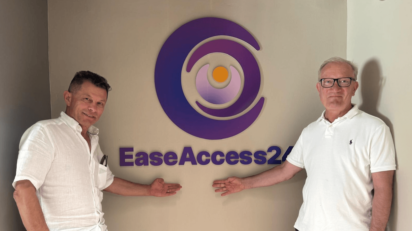 Two men standing beside and pointing at the EaseAccess24 logo on a wall.