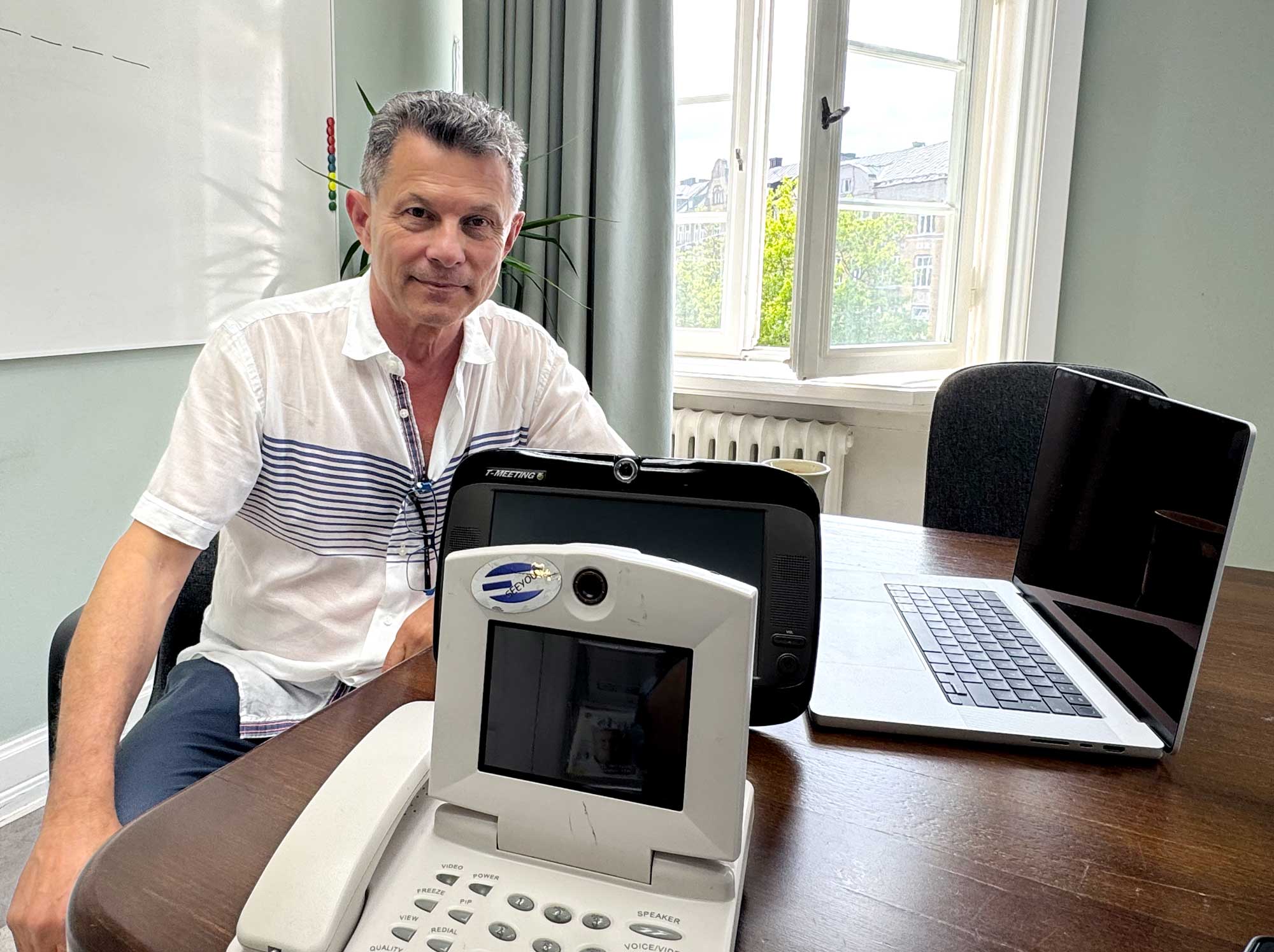 Max Tairi seated beside communication devices and a laptop.